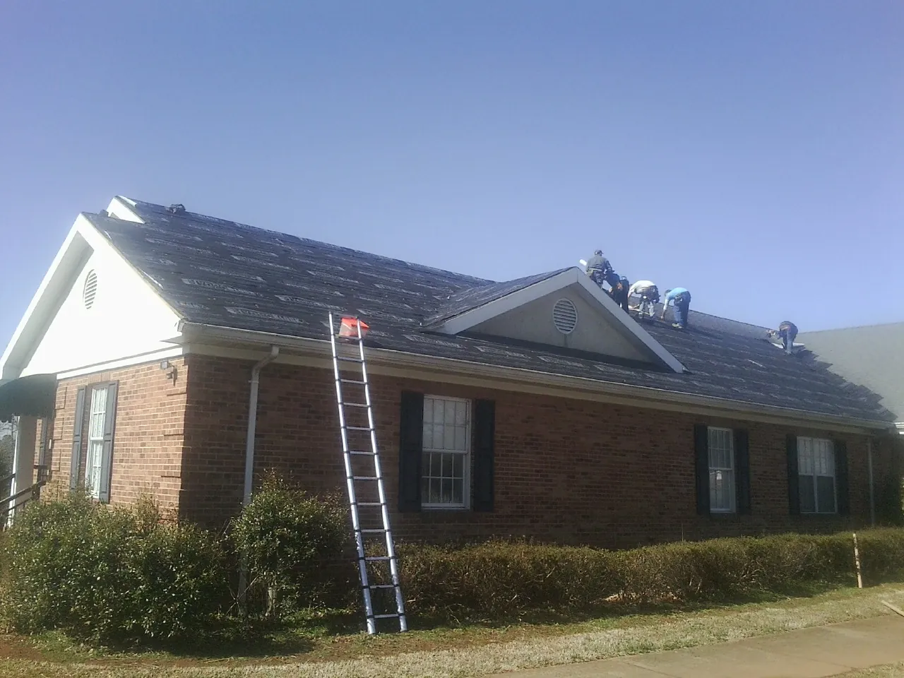 Crew tearing shingles off a brick ranch roof with a ladder set — Metal Roof Repair work by our crew in Elverson