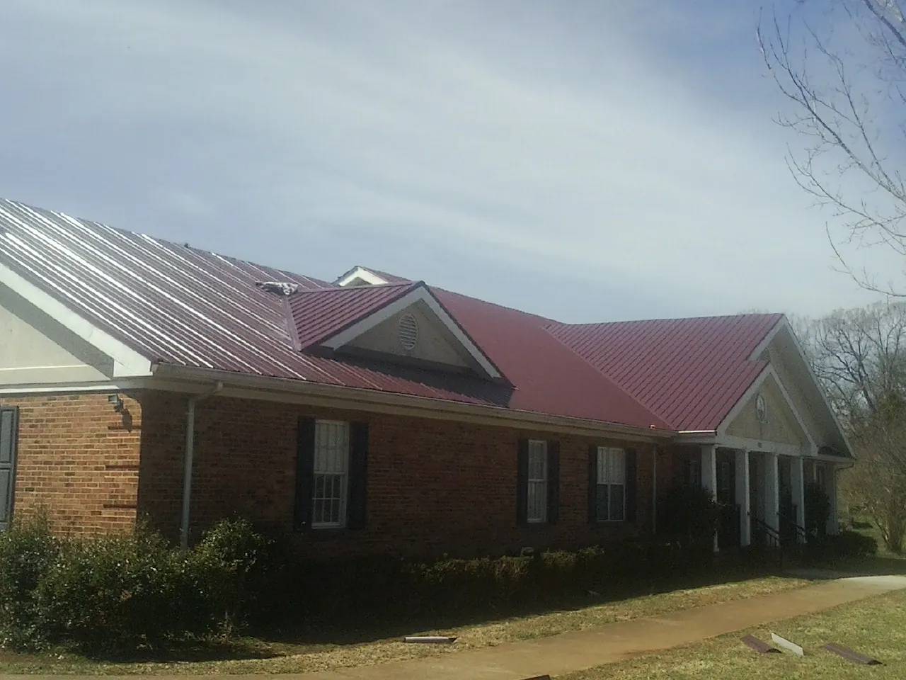 Red metal roof with gabled entries on a long brick building, from a Hail Damage Roof Repair job in Elverson