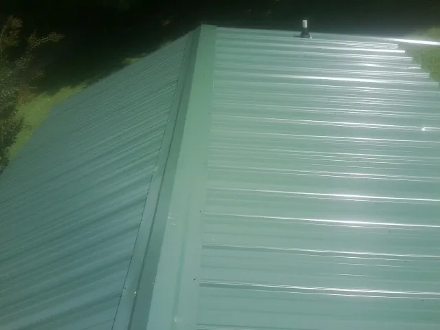 New green metal panels meeting at the ridge of a roof — Flat Roof Repair work by our crew in Elverson
