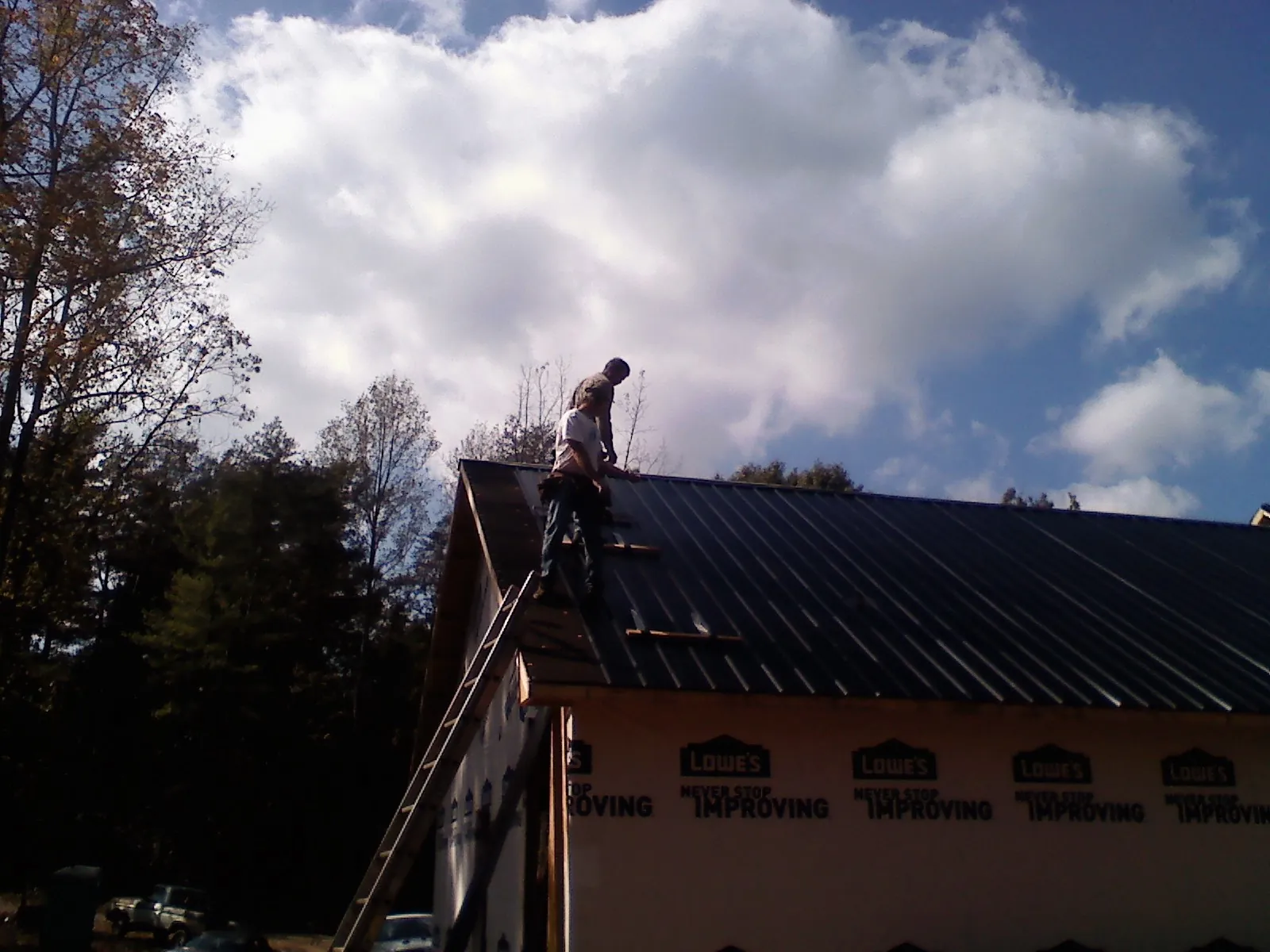 Roofer fastening dark metal panels high against a cloudy sky, from a Roof Inspection job in Elverson