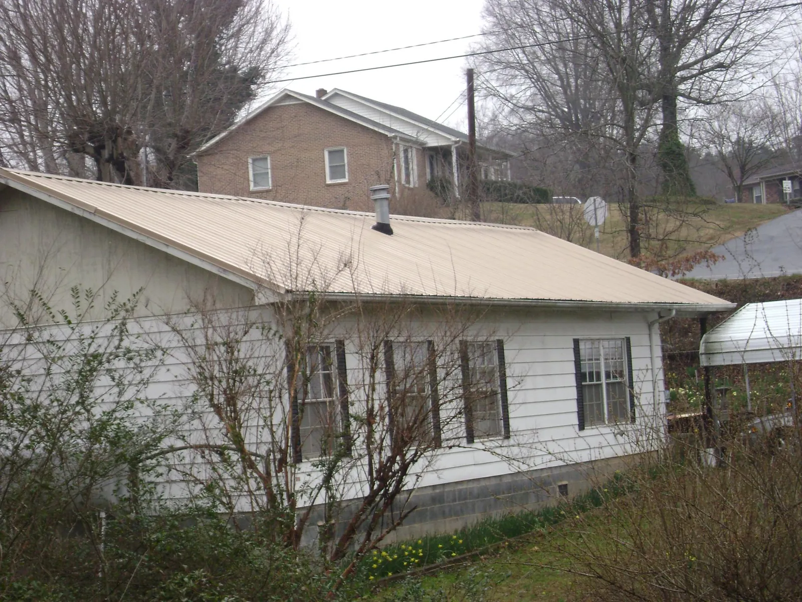 Tan metal roof on a white sided house set into a hillside — Commercial Roofing by Roofing Brothers in Elverson